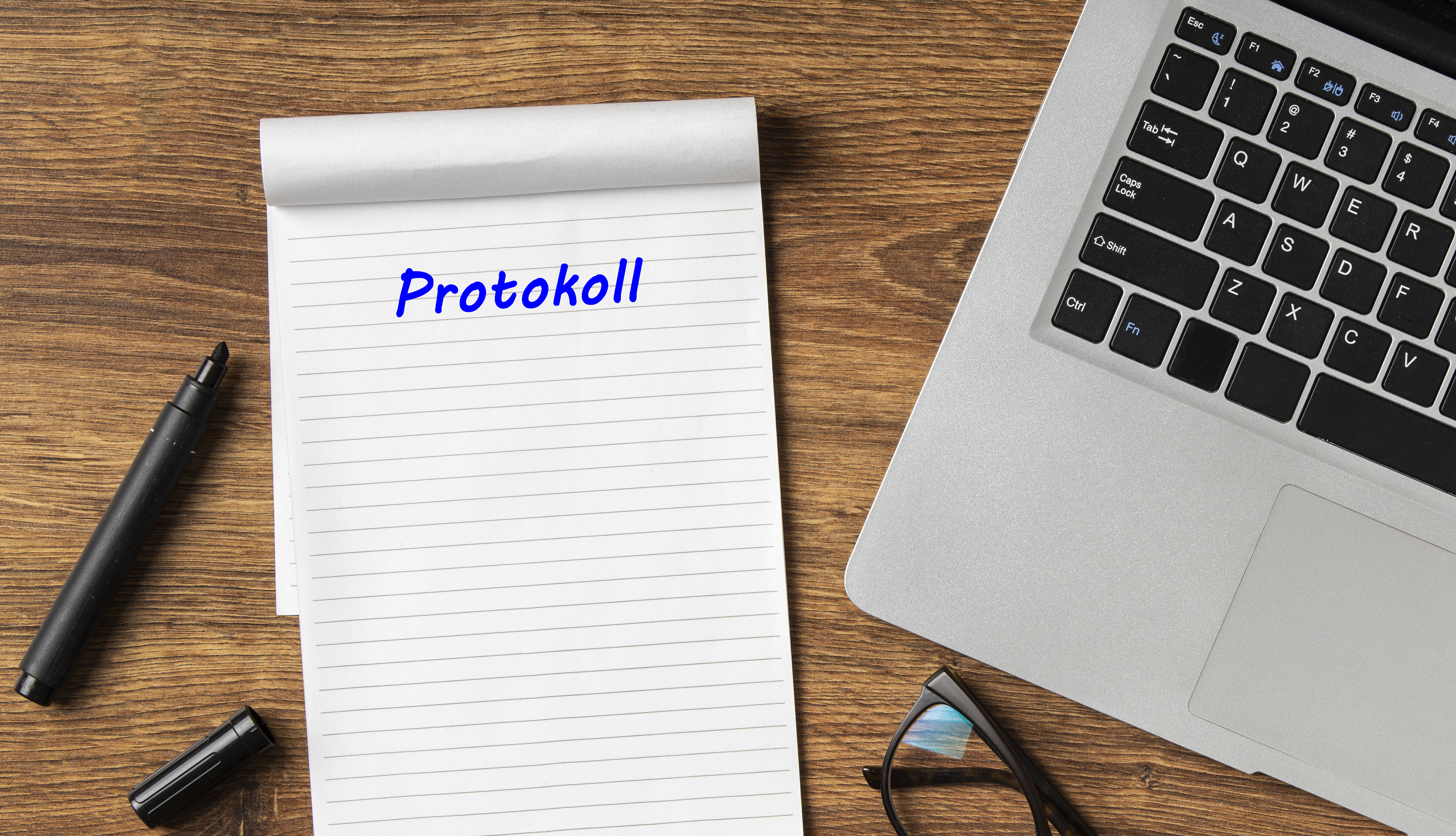 Das Bild zeigt einen Notizblock mit der Überschrift Protokoll und ein Tablet
