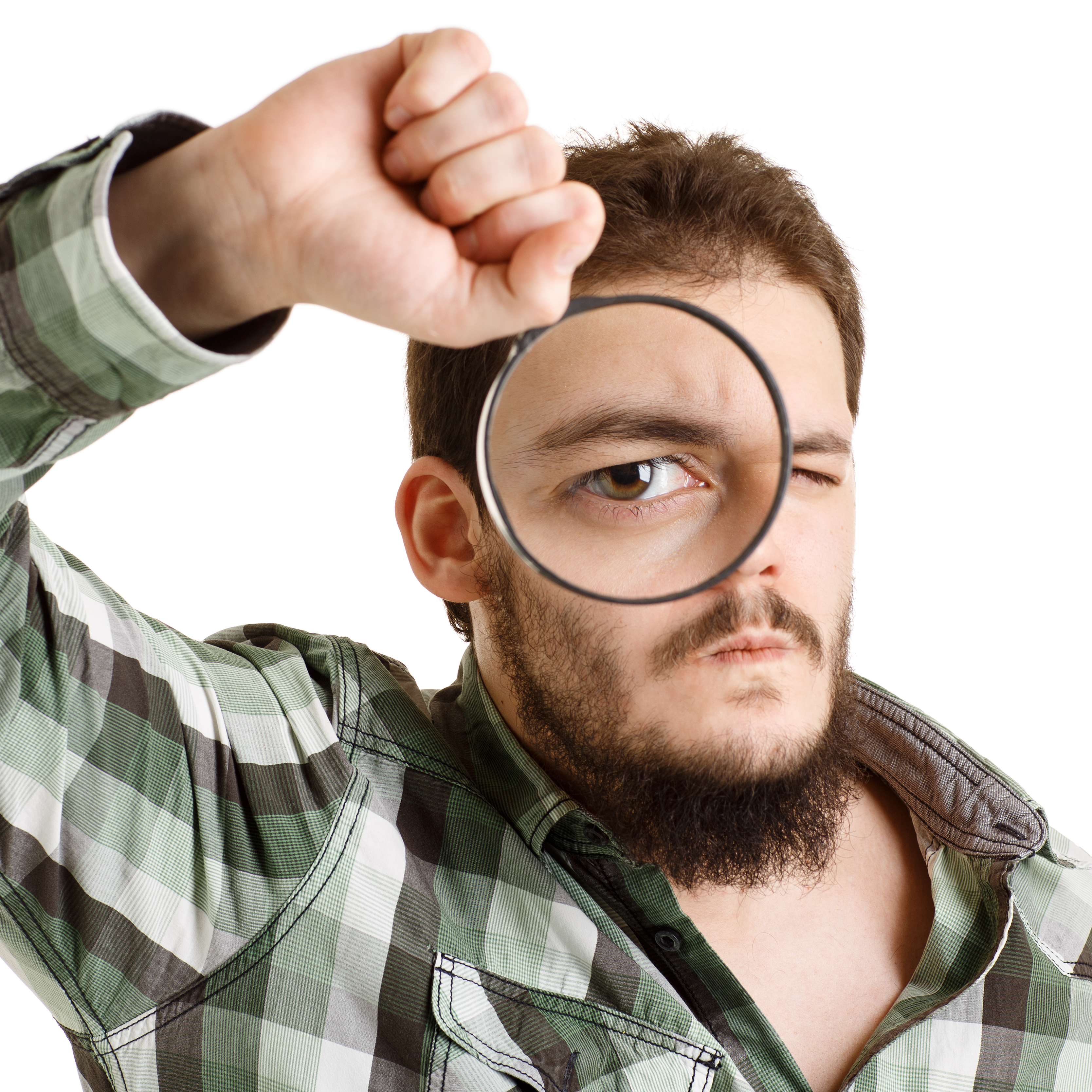 Das Bild zeigt einen jungen Mann , der durch ein großes Vergrößerungsglas zum Betrachter schaut und mit seinem durch das Glas vergrößerten Auge offensichtlich nach etwas sucht.